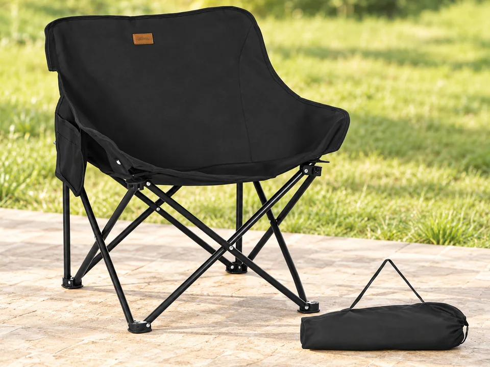 Outsunny — chaise basse enveloppante — Silhouette basse noire à dossier arrondi, petite étiquette brune, poche latérale et cadre noir en X conservés. Une chaise et un sac horizontal.