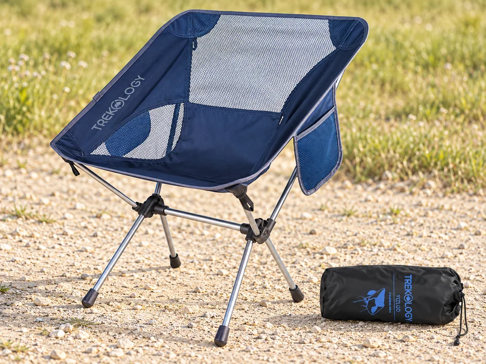 TREKOLOGY YIZI GO — chaise compacte — Coque bleu marine, panneaux de maille, poche latérale, raccords noirs et tubes argentés conformes. Housse posée au sol, main de la photo commerciale retirée.