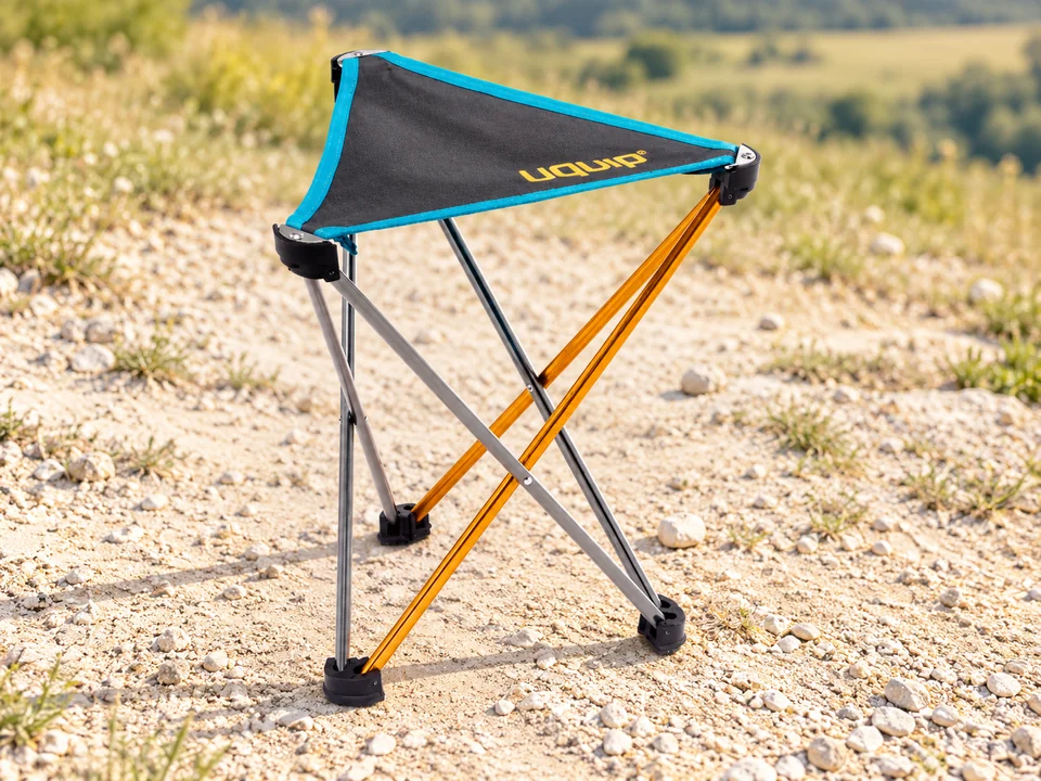 Uquip Trinity L — tabouret tripode — Assise triangulaire grise à bord turquoise, petit logo jaune, tubes argent et orange, trois appuis noirs reproduits sans dossier ni housse inventée.